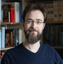 Bild von Nils Wiederer, der Autor und Betreiber von 3S+WebDesign. Freundlich lächelnder Mann Mitte Dreißig mit Brille, braunem Vollbart und braunem mittellangen Haaren, der vor einem Bücherregal sitzt.